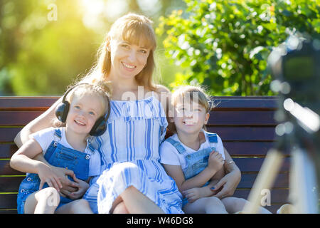 Une belle femme avec deux filles tourné en un programme TV, est assis en face d'un appareil photo sur un banc de parc. Banque D'Images