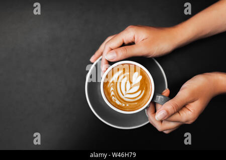 Tasse de cappuccino dans femme les mains sur fond de table en métal noir foncé. Lieu vide pour le texte. La dépendance du café. Vue de dessus dans un café branché. Banque D'Images