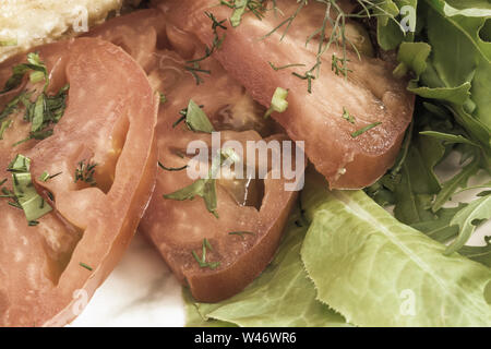 Sur une plaque trois tranches de tomates rouges mûres à côté d'une salade verte et le persil. Présenté en gros plan. Banque D'Images