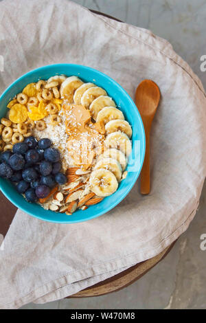 Délicieux petit déjeuner sain avec l'avoine, des petits fruits, amandes, bananes, beurre d'arachide et de céréales avec une cuillère de bois. Banque D'Images