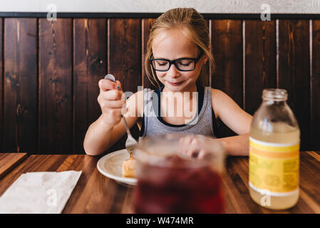 Petite fille mange et boit à table dans un café restaurant Banque D'Images