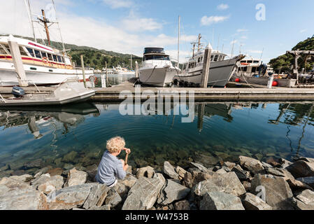 Bambin assis sur des rochers près de bateaux dans un port Banque D'Images