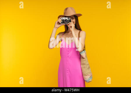 Happy girl dans une robe rose et lunettes de tenir l'appareil photo sur un fond jaune- image Banque D'Images