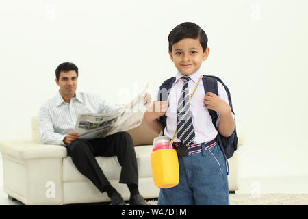 Portrait d'un écolier avec son père lisant le journal dans l'arrière-plan Banque D'Images