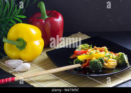 La nourriture asiatique, nouilles sautés avec légumes, sauce soja, poivrons et les ingrédients sur un tapis de bambou, fond noir Banque D'Images