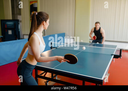 L'homme et la femme jouant au ping-pong à l'intérieur. Couple in sportswear détient les raquettes et joue au tennis de table dans une salle de sport Banque D'Images