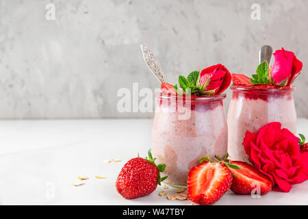 Saine alimentation. petit-déjeuner dessert du jour au lendemain l'avoine fraise avec les baies fraîches et menthe et fleurs de rose sur le marbre blanc table. close up Banque D'Images