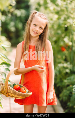 Cute little girl recueille les concombres et tomates de serre en Banque D'Images