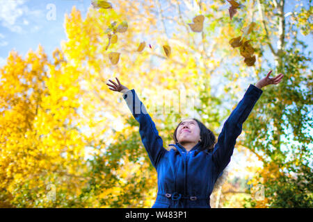 Asian teenage girl tossing en jaune des feuilles dans le parc avec des arbres couleurs changeantes au cours de l'automne. Banque D'Images