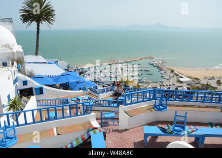 Un jeune couple Tunsian s'asseoir à une table de café donnant sur la mer Méditerranée et du port de l'aigue-marine dans la ville de Sidi Bou Said, Tunis, Tunisie. Banque D'Images