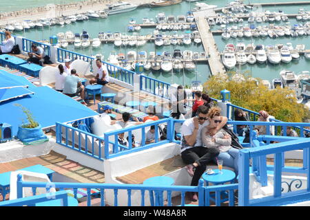 Un jeune couple Tunsian s'asseoir à une table de café donnant sur la mer Méditerranée et du port dans la ville de Sidi Bou Said, Tunis, Tunisie. Banque D'Images