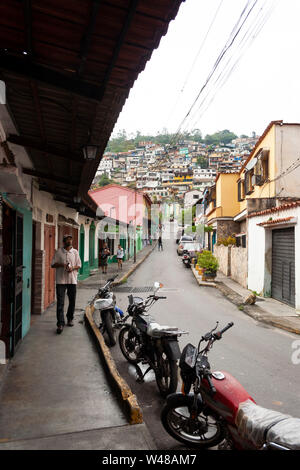 Vue sur rue étroite typique de El Hatillo, personnes marchant sur le trottoir, des motos garées l'une après l'autre et à l'avant sur la montagne certains sl Banque D'Images