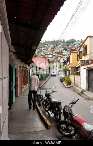 Vue sur rue étroite typique de El Hatillo, personnes marchant sur le trottoir, des motos garées l'une après l'autre et à l'avant sur la montagne certains sl Banque D'Images