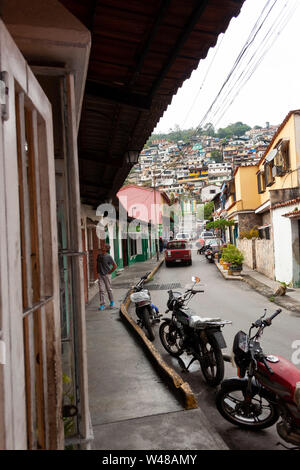 Vue sur rue étroite typique de El Hatillo, personnes marchant sur le trottoir, des motos garées l'une après l'autre et à l'avant sur la montagne certains sl Banque D'Images