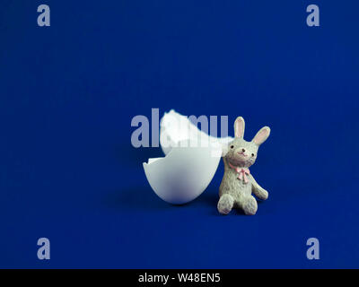 Lapin mignon avec poupée cassée de la coquille des œufs crack sur fond bleu, concept de Pâques Banque D'Images
