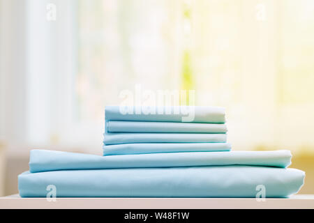 Close-up of blue literie propre sur un arrière-plan flou. Une pile de feuilles nouveau lit plié sur la table. La lumière du soleil de la fenêtre. Banque D'Images