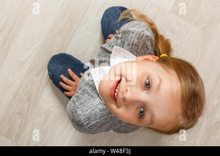 Vue de dessus d'un enfant assis sur le plancher. La petite fille leva la tête vers le haut et à la recherche dans l'appareil. Banque D'Images