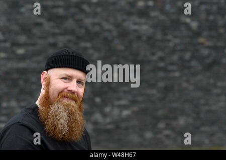 Heureux l'homme à barbe rousse touffue et les yeux bleus portant un Beanie Hat smiling at the camera sur un fond gris Banque D'Images