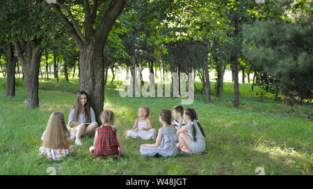 Les enfants et l'éducation, jeune femme au travail comme éducateur lecture livre pour garçons et filles en parc. Banque D'Images