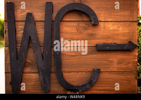 Inscription WC sur une planche de bois. Pointeur de toilettes, panneau. Texte de lettres noires. La texture du bois brun. Banque D'Images