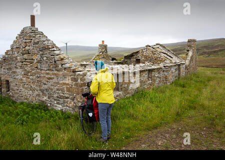 Une éolienne sur croft avec Rousay, îles Orkney, Scotland, UK avec une femme cyclotourisme. Banque D'Images