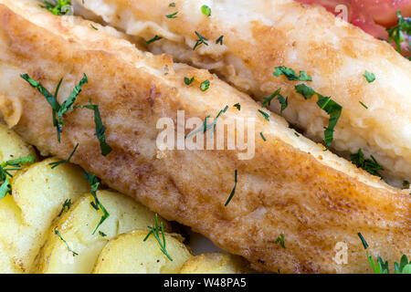 Sur la table sur une assiette deux tranches de poisson frit, des pommes de terre sautées , aneth, persil. Présenté en gros plan. Banque D'Images
