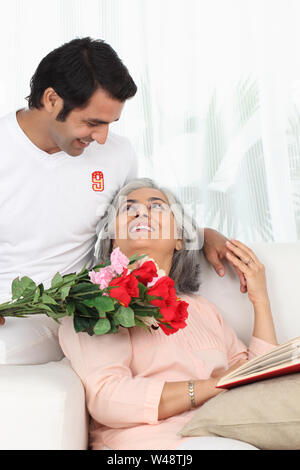 Homme donnant un bouquet de fleurs à sa mère lisant un livre Banque D'Images