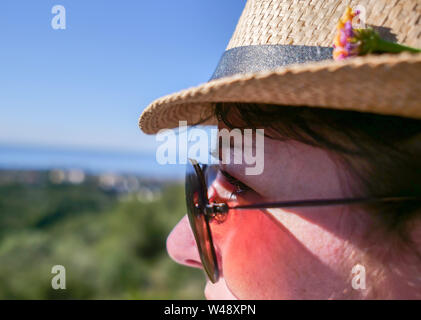 Jolie fille brune à lunettes de soleil et un chapeau avec une fleur regarde ailleurs Banque D'Images
