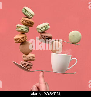 Parfait équilibre concept toujours la vie sur fond de papier de couleur corail. L'équilibre entre tasse de café et macarons sur un doigt. Banque D'Images