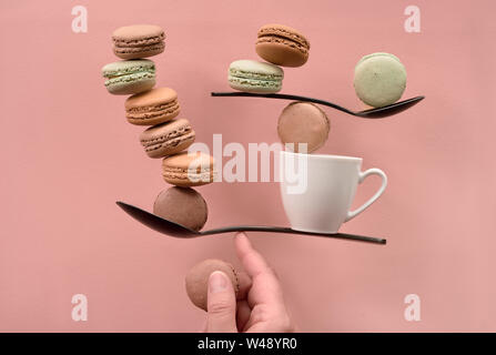 Concept d'équilibre télévision jeter sur papier couleur corail. L'équilibre entre tasse de café et macarons sur un doigt Banque D'Images