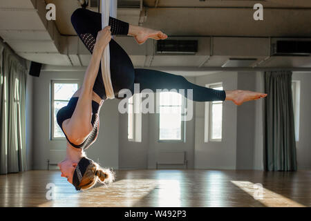 Belle fille yoga aérienne animateur illustre medutiruet sur lignes suspendus la tête en bas dans une salle de yoga. Concept yoga, corps souple, mode de vie sain Banque D'Images