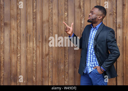 L'homme noir africain avec barbe l'opposé côté avec doigt sur fond de bois. Il est sérieux et regarde ailleurs, copyspace Banque D'Images
