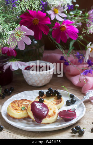 Petit-déjeuner de crêpes, quark, crème de cassis et groseilles un bouquet de fleurs sauvages sur un fond de bois. Banque D'Images