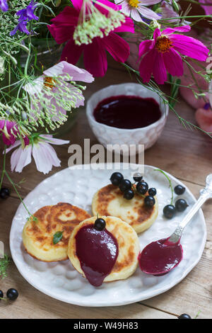 Petit-déjeuner de crêpes, quark, crème de cassis et groseilles un bouquet de fleurs sauvages sur un fond de bois. Banque D'Images