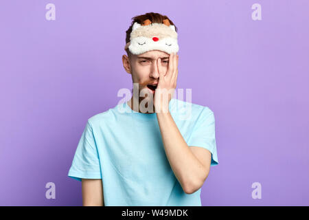 Sleepy fatigué barbu avec creative moustache avec un Palm sur hs joue au décollage ou la mise sur le masque de sommeil. close up portrait of blue isolés. Banque D'Images