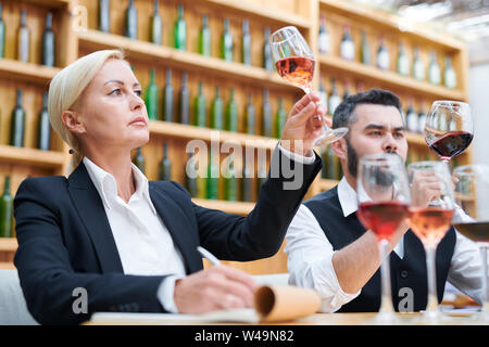 Sommelier femelle et son collègue en soirée à la recherche au vin dans bokals Banque D'Images