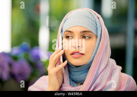 Jeune femme musulmane hijab en conversation sur smartphone outdoors Banque D'Images