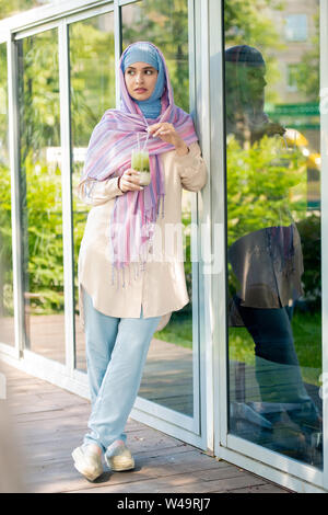 Jolie jeune femme sereine dans casualwear et hijab avoir verre sur terrasse Banque D'Images