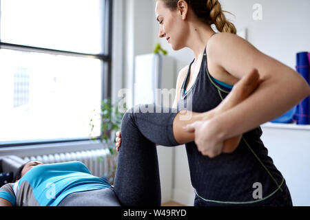 Caucasian woman physiothérapeute strectching la jambe et du genou d'un mid-adult chinese female patient assis sur une table de massage Banque D'Images