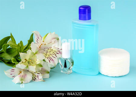 Le flacon en verre avec vernis incolore, bouteille en plastique avec du vernis à ongles, dissolvant les tampons de coton et de fleurs blanches sur fond bleu. Banque D'Images