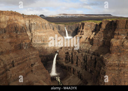 Cascade majestueuse en cascade dans le canyon accidenté entouré de montagnes enneigées dans le plateau de Putorana, au nord de la Russie, réserve naturelle de Putoranskiy. Banque D'Images