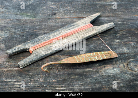 S'attaquer à l'ancienne pour clignotant vertical les poissons prédateurs. Forgé cuivre spinner et le tambour en bois avec corde sur fond rustique. Banque D'Images