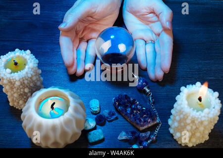 Mains d'une cartomancienne travaillant avec une boule de cristal dans la lumière bleue Banque D'Images