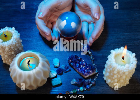 Mains d'une cartomancienne travaillant avec une boule de cristal dans la lumière bleue Banque D'Images