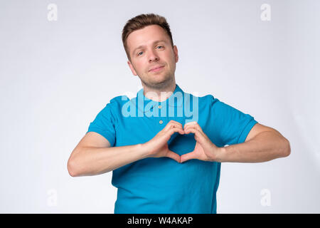 Bel homme en chemise bleue faisant un coeur avec ses mains Banque D'Images