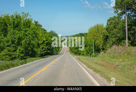 Route vallonnée dans une journée de printemps ensoleillée, campagne. L'autoroute nationale vide passant à travers le feuillage frais printemps arbres, Texas, États-Unis Banque D'Images