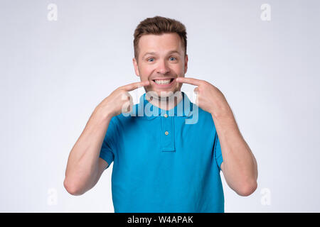 Jeune homme européen en bleu t-shirt affiche sur ses dents. Banque D'Images