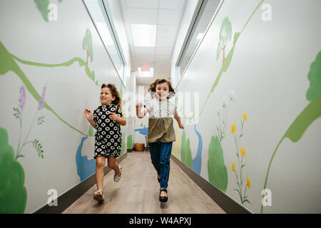 Deux filles sourire et courir dans un couloir dans un bâtiment scolaire Banque D'Images