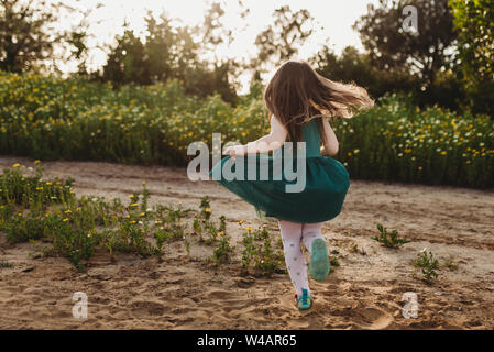 Petite fille faisant tournoyer sa robe dans le rétroéclairage et champ de fleurs Banque D'Images