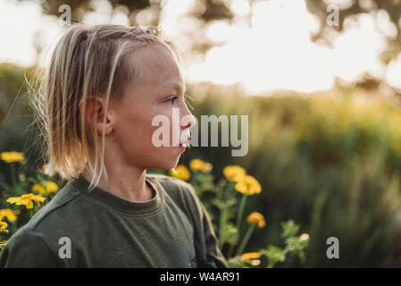 Vue latérale du jeune garçon aux cheveux longs dans le champ de fleurs Banque D'Images